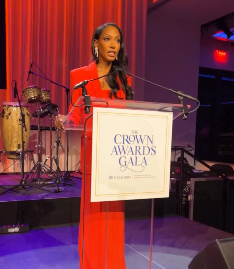 A woman in an orange dress speaking at a podium labeled the crown awards gala at columbia with a music set in the background.